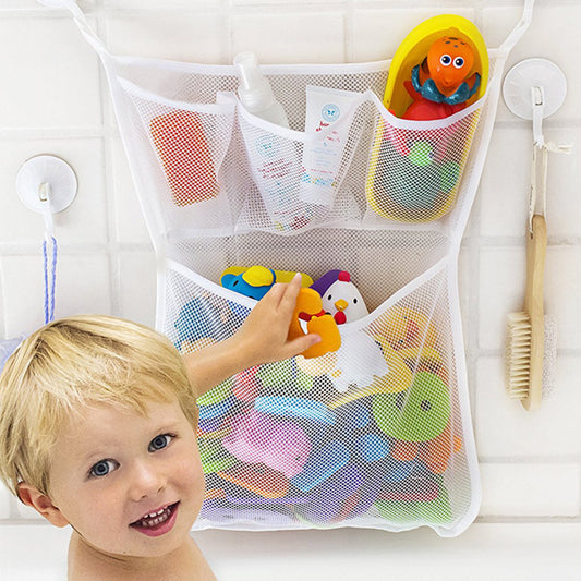 Child playing with bath toys in a mesh storage bag on a white wall.