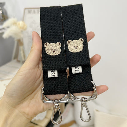 Black strap with bear face designs held by a hand against a blurred indoor background